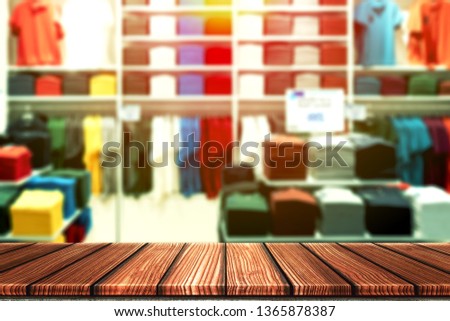 Wooden table with blurry background of casual boutique shop, shirt brand outlet or colorful clothes store for product display montage. Retail business of fashion product for online marketing backdrop.