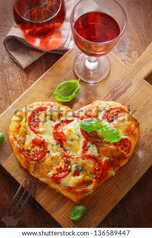 Overhead view of a tasty cheese and tomato vegetarian heart shaped pizza served on a wooden board with a glass of red wine