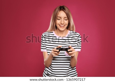 Emotional young woman playing video games with controller on color background