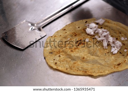 
Indian street food vendor make,adding onion pieces  ingredient while frying wheat roti or flat bread on pan in oil                               