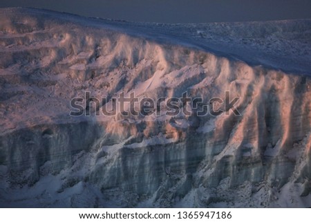 Close picture of an iceberg, texture of an ice layers and snow cover. Landscape of the wild nature in winter, cold region. Sun rays laying on the surface.