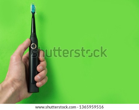 Electric sonic toothbrush in hand on green color background with copyspace