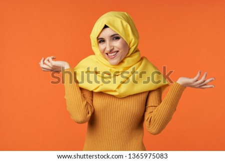 Funny cute Muslim woman with yellow hijab spreads her arms orange background Indonesia Islam
