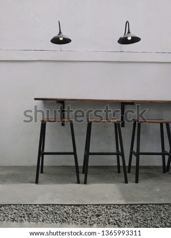 
A picture of three chairs, a table, and two chandeliers with white walls as the backgrounds..
