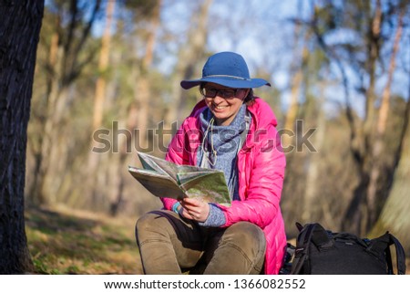 female tourist in the forest looks at a map sitting on a stump