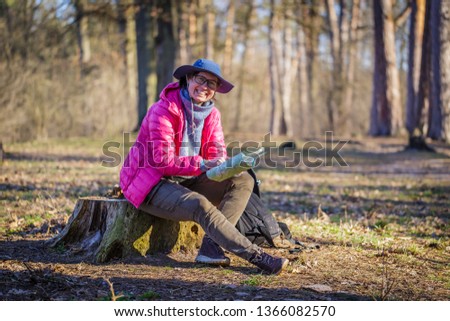 female tourist in the forest looks at a map sitting on a stump
