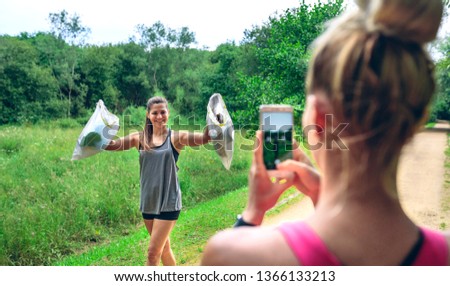 Girl taking a picture of a friend with trash bags after plogging. Selective focus on girl in background