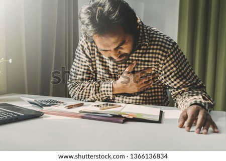 office syndrome concept; businessman sitting at office desk,  suffering from backache after working,man touching lower back with pained expression.
