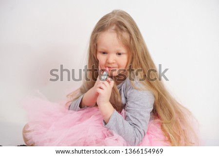 a little caucasian blonde girl sits and do make up with her mother's pink lipstick and wants to become an adult sooner