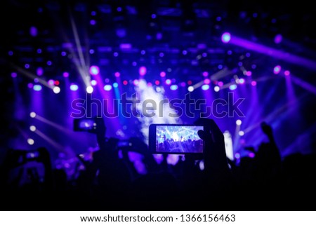 Smartphone in hand at a concert, blue light from stage.