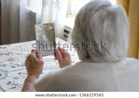 Older woman looking to the photo with young herself. Vintage photos, nostalgie