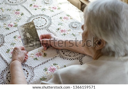 Older woman looking to the photo with young herself. Vintage photos, nostalgie