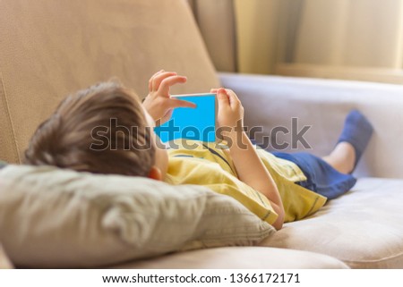 Little cute boy in a yellow T-shirt playing games on a tablet and watching cartoons. Toddler with smartphone. Little boy using smartphone at home. 