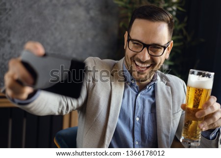 Young smiling businessman drinking beer and taking a selfie in a cafe