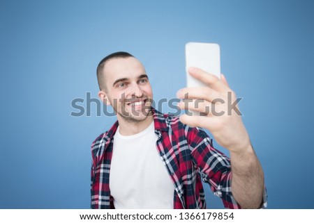 Bearded young man smiling and posing for selfie, front view, blue background, copy space