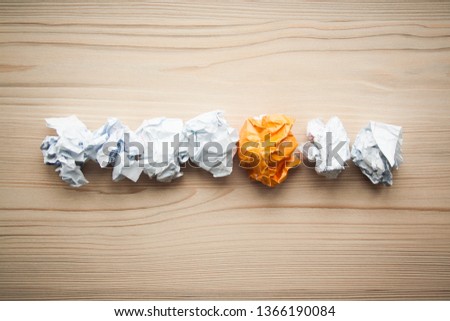 Line of crumpled white paper balls with one different orange paper ball between them. Concept of think different, think out of the box, leadership. 