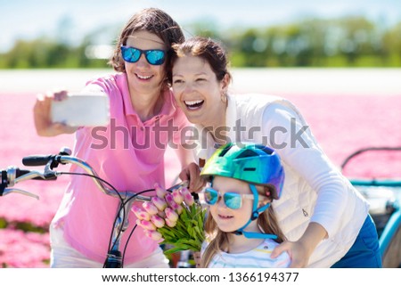 Dutch family riding bicycle in tulip flower fields in Netherlands. Mother and kids taking selfie picture with mobile phone camera on bikes at blooming tulips in Holland. Parents and children biking.