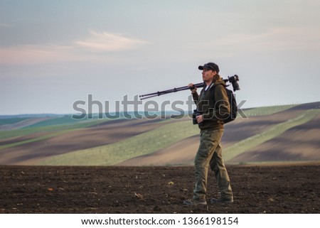 Outdoor wildlife photographer with camera, tripod and binoculars looking for animals in nature. Rural scene know as Moravian Tuscany at Czech Republic