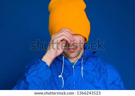  young man in a blue sport 90s style jacket and yellow hat portrait ,man hiding his face under  cap