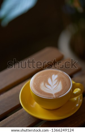 Latte in a yellow cup on wooden table . Top view.