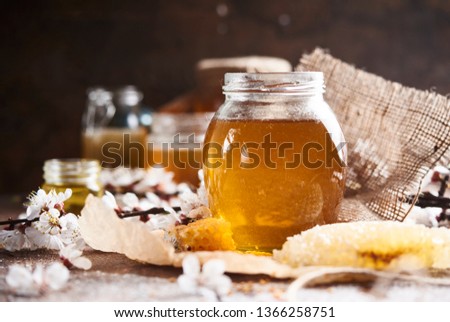Sweet fresh Hohey in glass jar with  honeycomb, wooden dipper and flowers over dark wooden background.