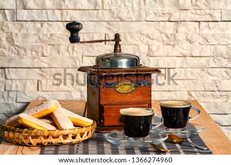 Old vintage coffee grinder on the wooden table an white brick wall background, two cups of coffee and cake.