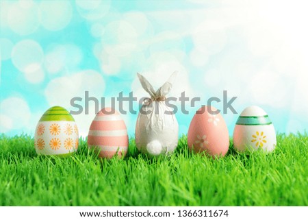 Easter egg wrapped in a paper in the shape of a bunny with colorful Easter eggs on green grass. Spring holidays concept.