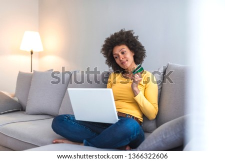 Internet payment. Happy cheerful woman looking at the Internet screen while making an Internet payment. Happy young woman with credit card and laptop sitting on sofa at home. Online payment 