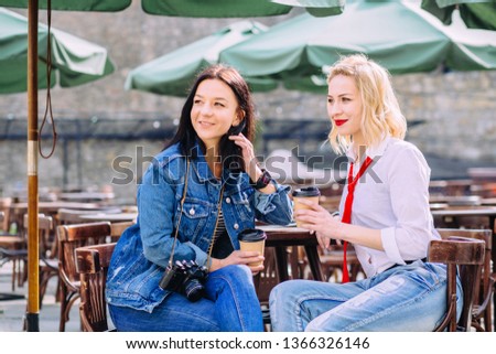 Portrait of two young women sitting together drinking coffee in summer street cafe. Girls photographing themselves with retro camera.