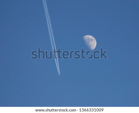 Flight past a silvery winter moon leaving a vapor trail. 
