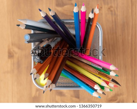 Colorful pencils for creativity in a metal mesh cup on the background of a wooden table.