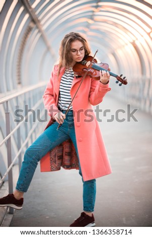 Young woman in pink coat standing on the overhead passage playing violin