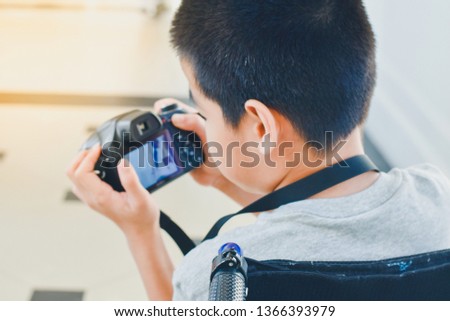 Photographer child on wheelchair is holding a camera in hand, He was smiling and having fun with it,Life in the education age of disabled children, Happy disabled kid concept.