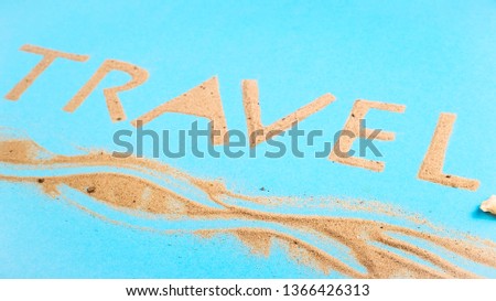The word travel written on a bright blue background of beach sand - a vacation at sea concept. Top view, flat lay