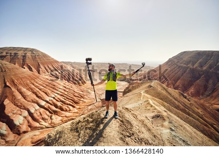 Bearded man holding two cameras on the top of the mountain in the desert 