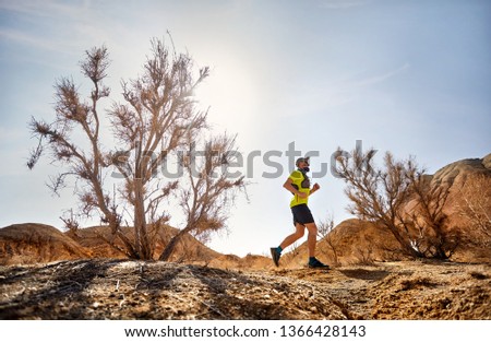 Runner athlete with beard running on the wild trail at red mountains in the desert