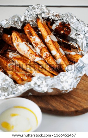 Homemade caramelized roasted in foil sliced yams or sweet potato with Greek-style yogurt and crushed red-pepper flakes close-up on white wooden background.Healthy vegetable yummy side-dish