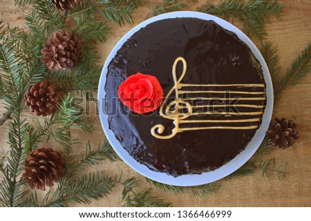 Top View Of A Chocolate Cake With A Stylized Image Of A Musical Staff (Stave) With A G-Clef And A Red Rose On A Wooden Background