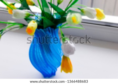 pictured in the photo Artificial yellow tulip flowers at blue vase,, the image does not focus and blurred