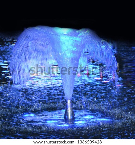 A small water fountain with blue backlighting at night. Image