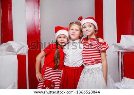 Little cute girls in studio with winter holiday decoration and props. Beautiful girls in funny Christmas clothes have fun, lively emotions.