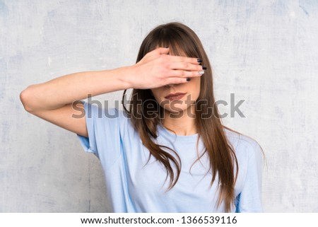 Young woman on grunge background covering eyes by hands