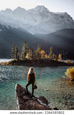 Young blonde girl standing on a stone and watching the beautiful sunrise in autumn at famous Eibsee lake,Germany