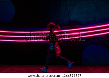 Unrecognizable girl running in front of 3 vivid pink LED tube lights. Motion blur. Night life. Abstract background with copy space