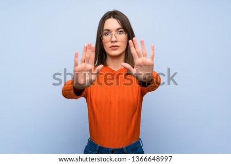 Teenager girl over blue wall making stop gesture and disappointed