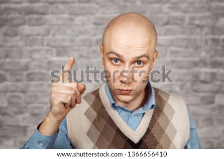 Portrait Bald serious man points and threatens with forefinger on brick wall white background.