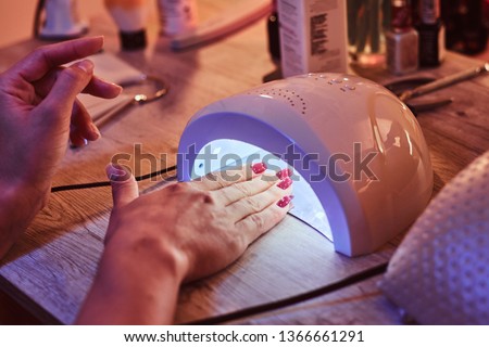 Client with red varnish at manicure salon cairfully waiting when her nails become dry  in UV light. Closeup shoot. Royalty-Free Stock Photo #1366661291