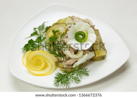 original salad with meat and pickled cucumbers, on a white plate, on the table