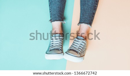 Women's legs in tight, torn jeans, sneakers on yellow blue pastel background. Top view, minimalism, copy space