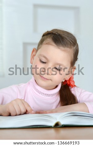 little cute girl reading a book at a table at home